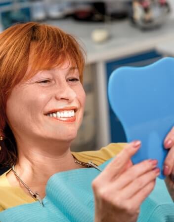 Woman with red hair admiring her new veneers with a mirror