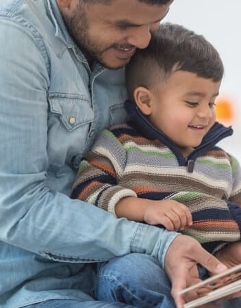 A father reading to his son who is sitting in his lap smiling