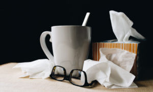 Closeup of a box of tissues, a used tissue, glasses, and a mug because someone is sick with a cold or flu