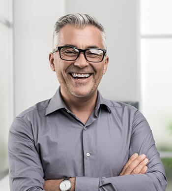 Older man with gray hair smiling with his arms folded