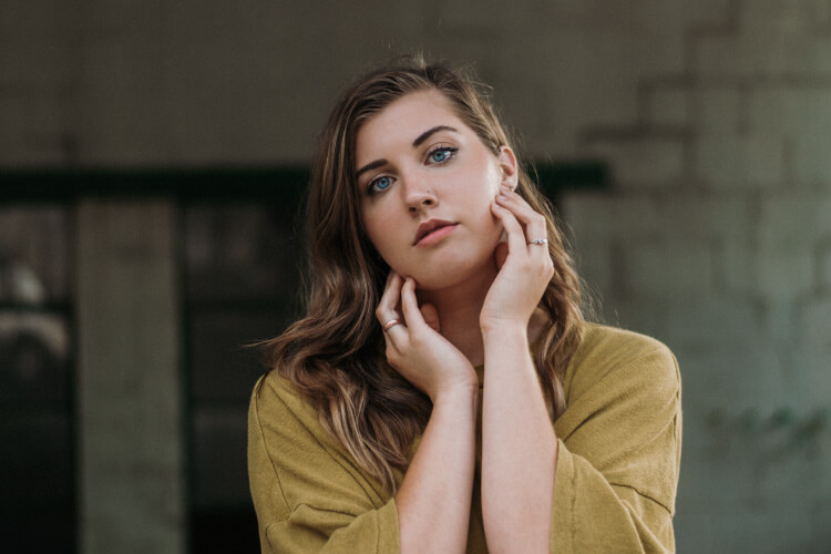 Brunette woman wearing a yellow blouse touches her cheeks in pain due to tooth sensitivity