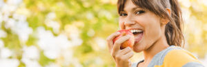 Young brunette girl eating an apple outside after root canal