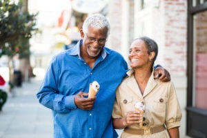 An older husband and wife with dentures smile as they walk down the sidewalk with ice cream cones