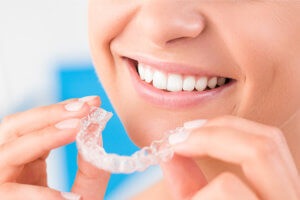 Closeup of woman smiling as she puts in her Invisalign trays to straighten her teeth in Long Island City, NY