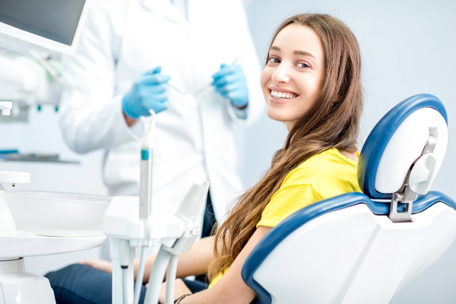 Brunette woman in a yellow shirt smiles while sitting in the dentist's chair after root canal therapy