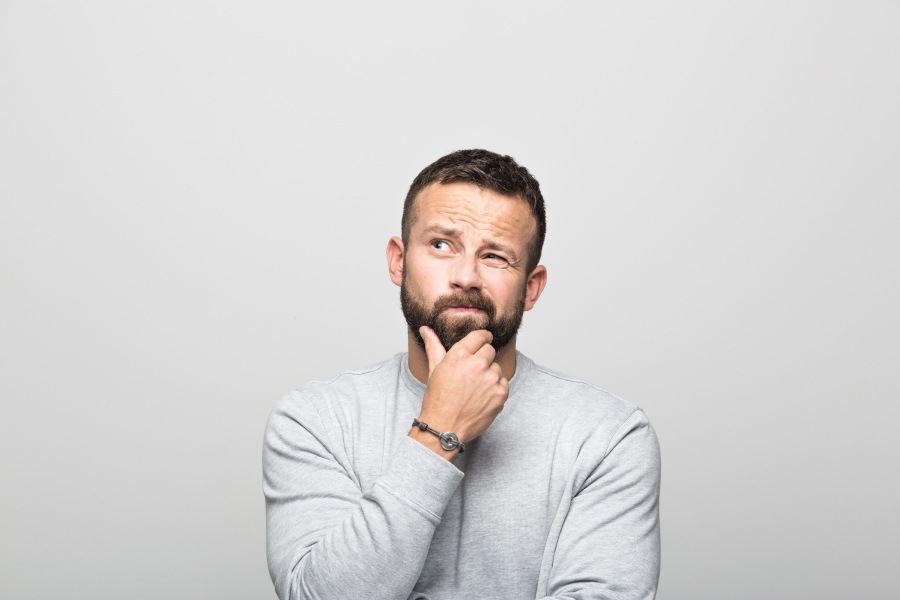 Brunette man with a beard and gray shirt wonders is it safe to visit the dentist during the pandemic