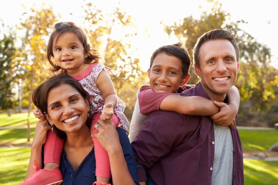 Mom and dad smile as they give piggyback rides to their 2 children to help them deal with dental anxiety