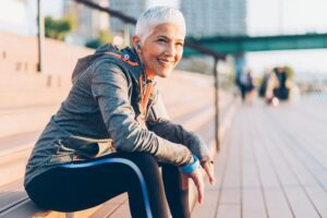 Fit older woman in workout clothes sitting on the steps outside.