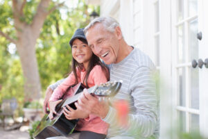 Grandpa playing the guitar on the porch with his young granddaughter.