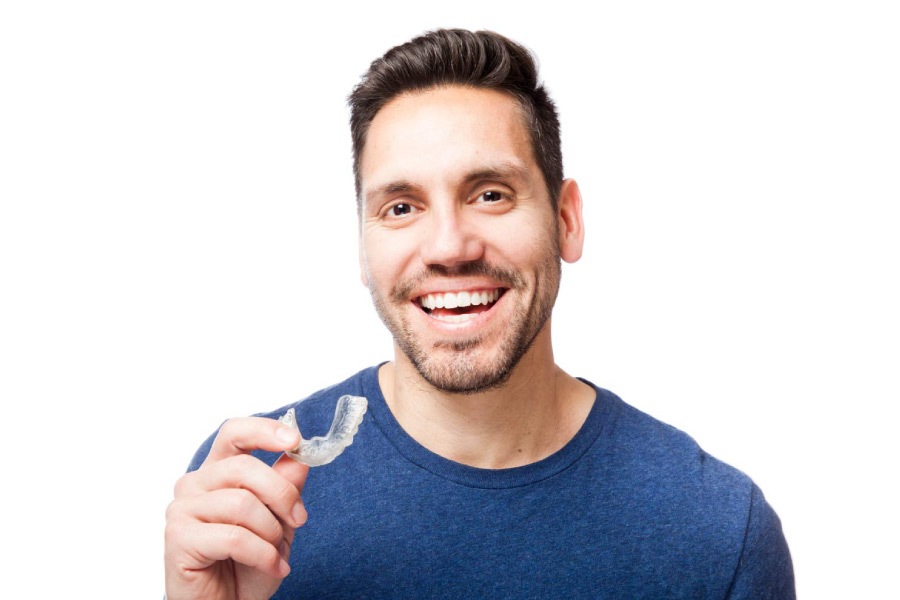 Smiling man holding a clear Invisalign aligner.