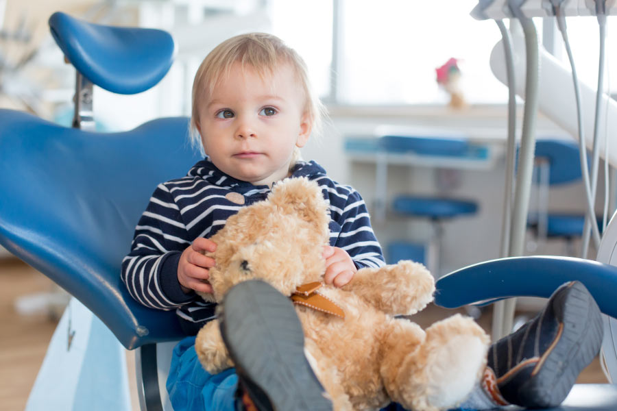 Toddler boy in the dentist chair with his stuffed bear.