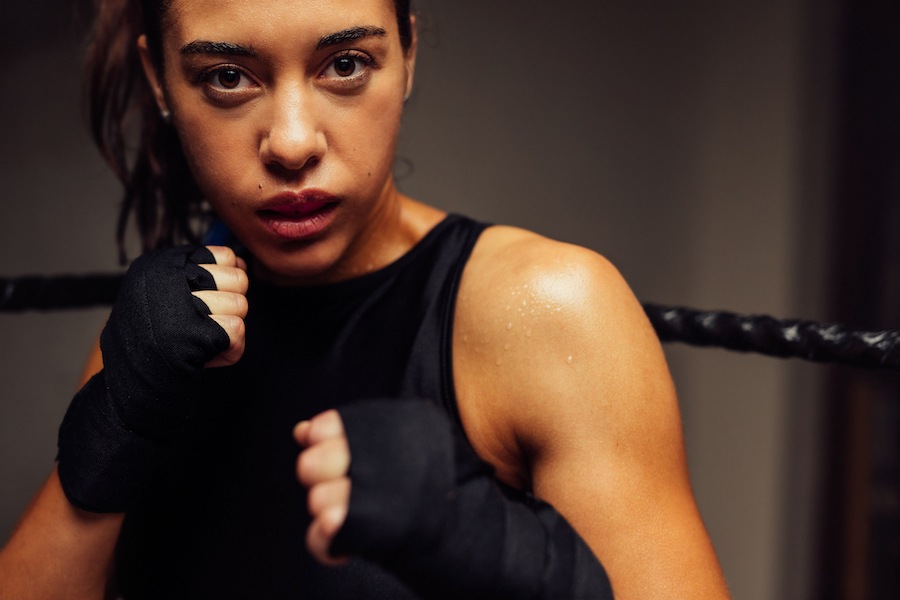 athletic mouthguard, Female martial artist looking at the camera while standing in fighting position inside a boxing ring. Female boxer training in a boxing gym.